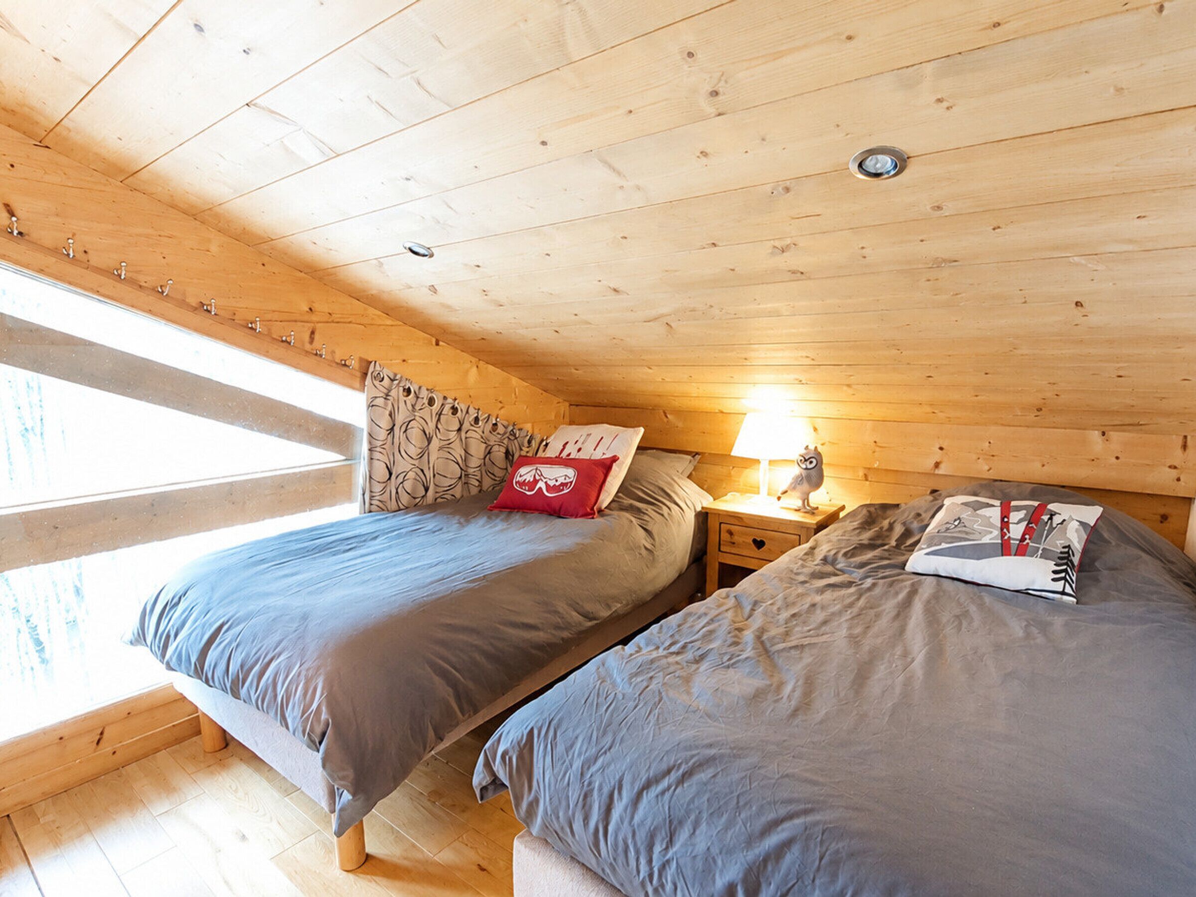 Une chambre confortable dans un chalet, avec deux lits, une table de chevet avec une lampe et une fenêtre avec des rideaux.