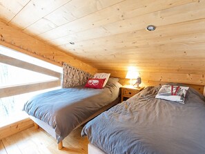 Een gezellig slaapkamer in een chalet met twee bedden, een nachtkastje met een lamp en een raam met gordijnen.