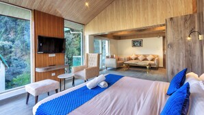 Un dormitorio moderno con una cama grande, un televisor, un espacio de descanso con sillas y vistas al exterior.