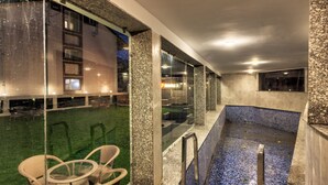 Un área de piscina con paredes de vidrio, una piscina pequeña y mobiliario exterior.