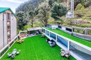 Un patio exterior moderno con piscina, zonas de estar y vistas a un paisaje montañoso.