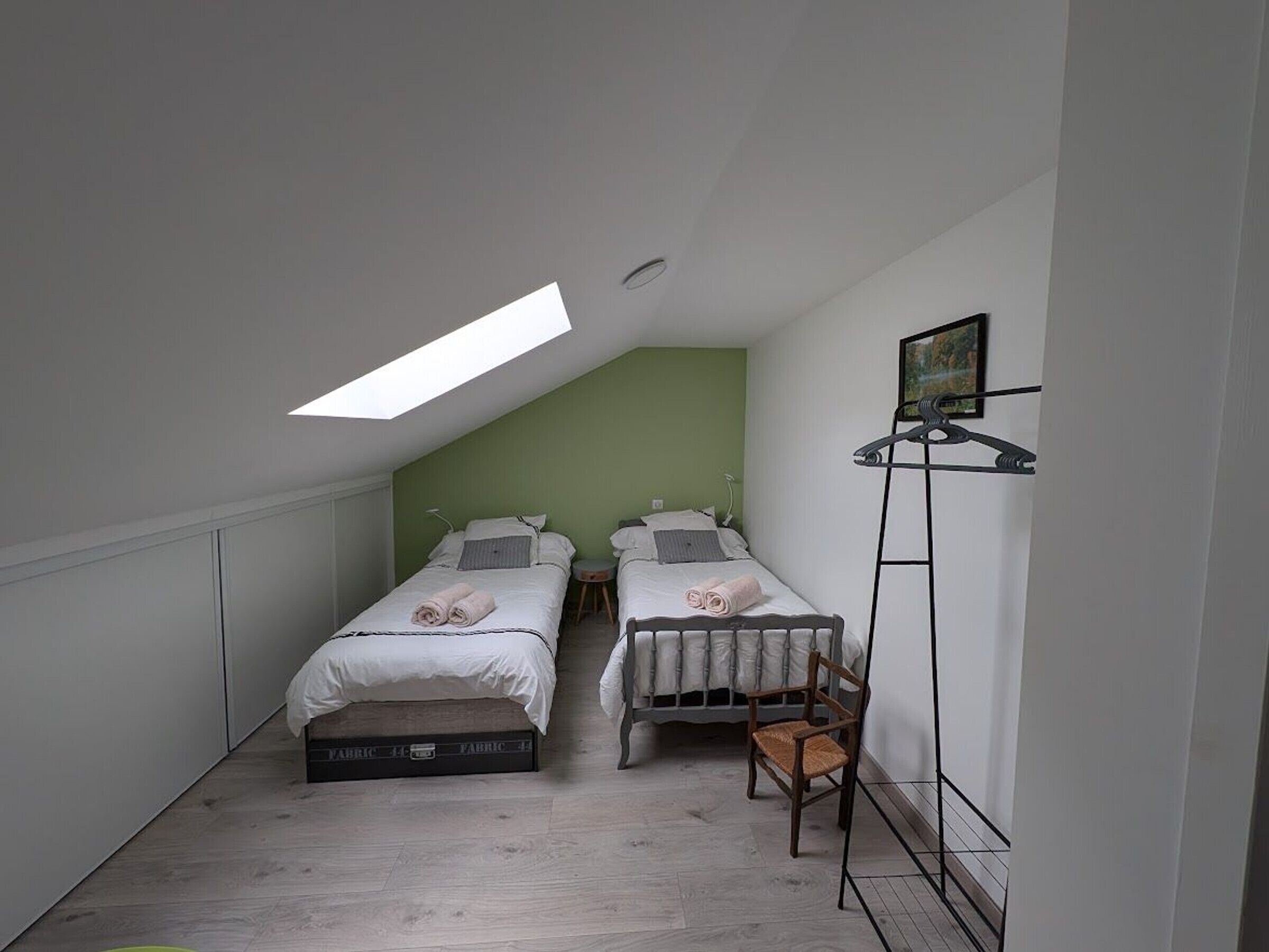 Un alojamiento pequeño, con una habitación individual, dos camas, un tragaluz, una silla y un radiador.