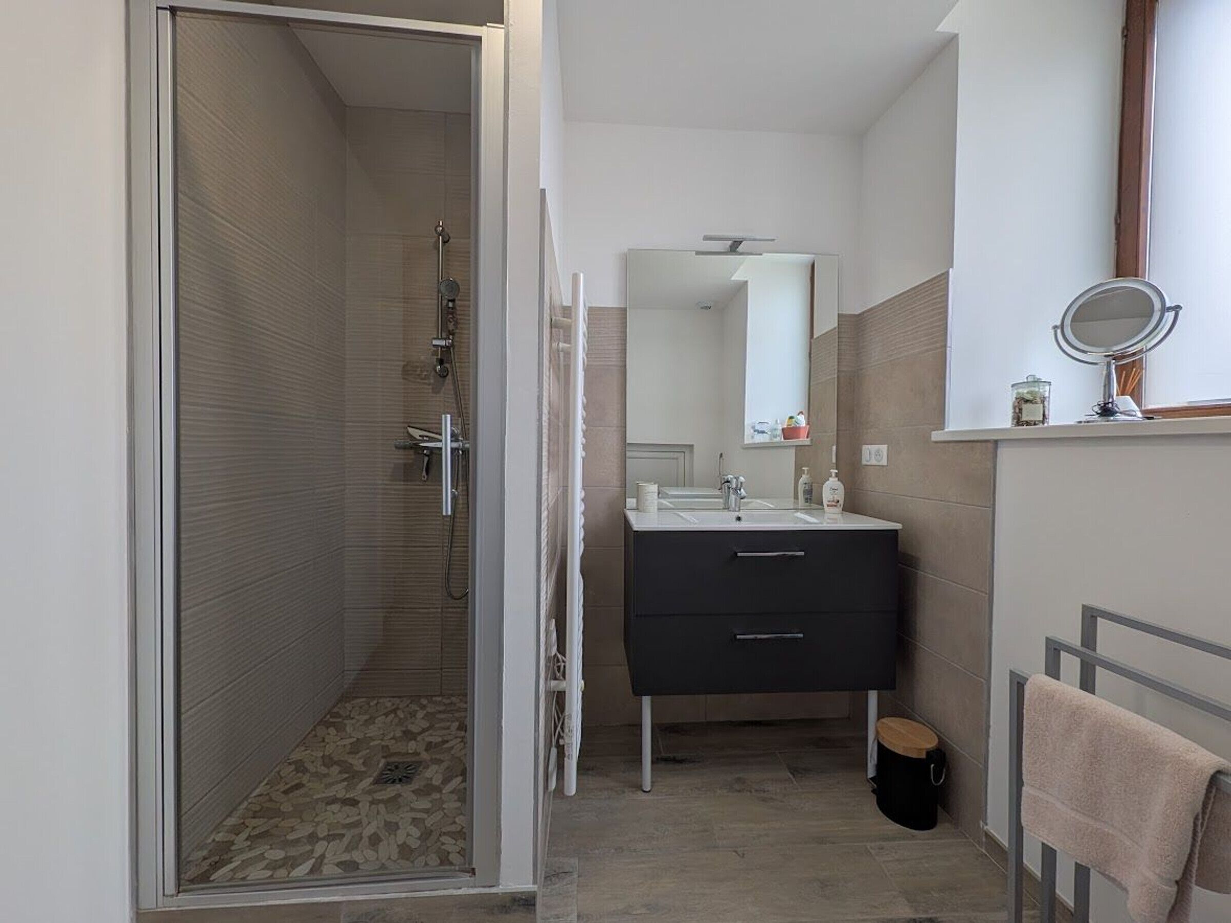 Une salle de bain moderne équipée d’une douche, d’un lavabo avec un miroir et d’un porte-serviettes.