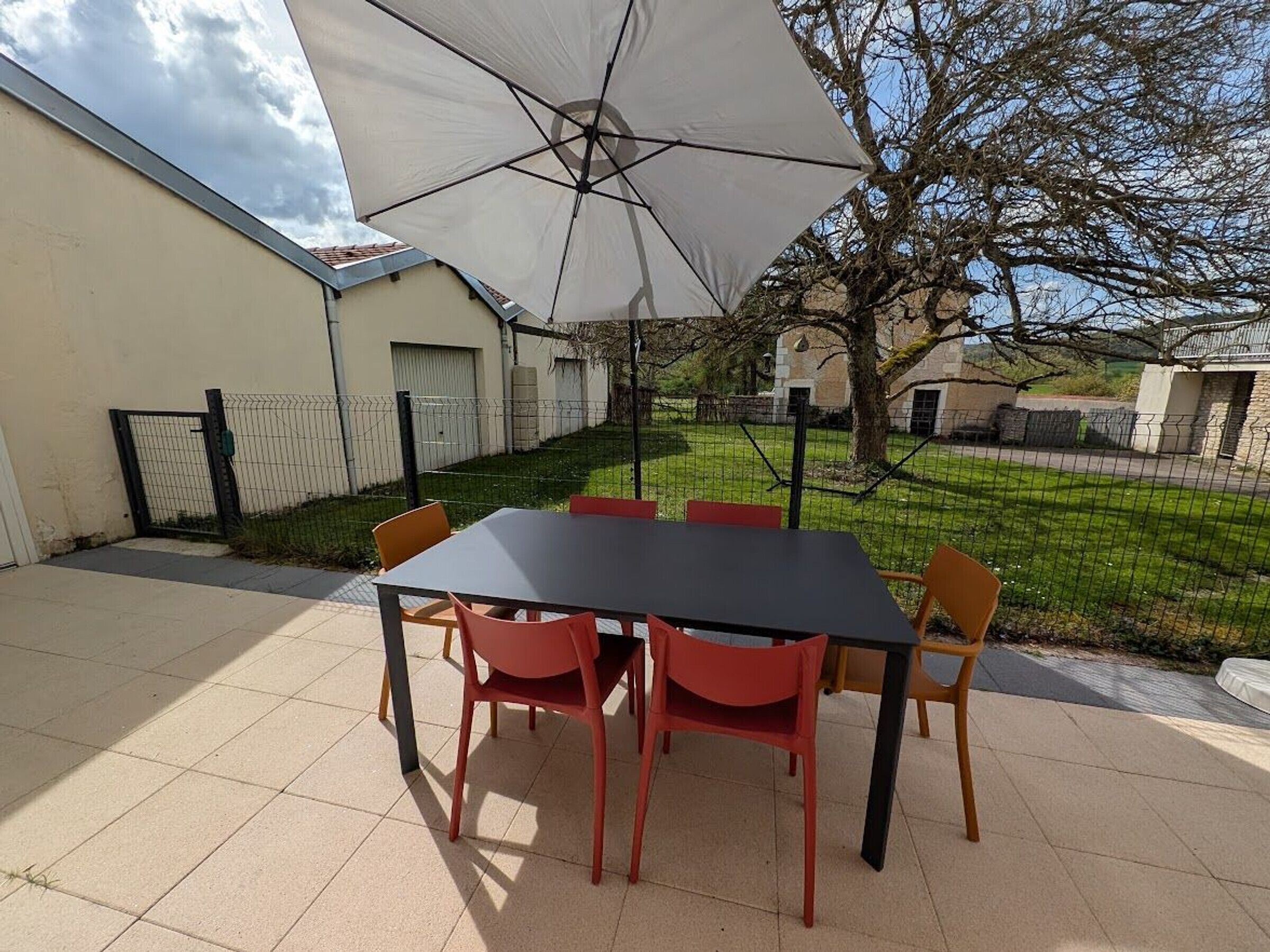 An outdoor patio with a table and chairs, a large umbrella, and a fenced yard.