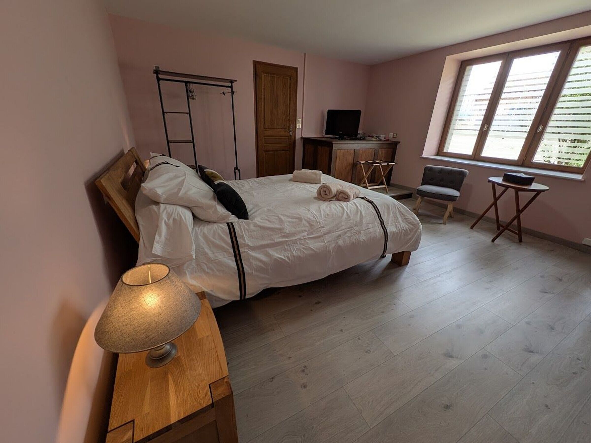 Een slaapkamer met een bed, een bureau, een stoel, een lamp en een raam.