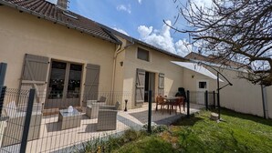 A house with a tiled roof, a fenced patio with outdoor furniture, and a clear sky.