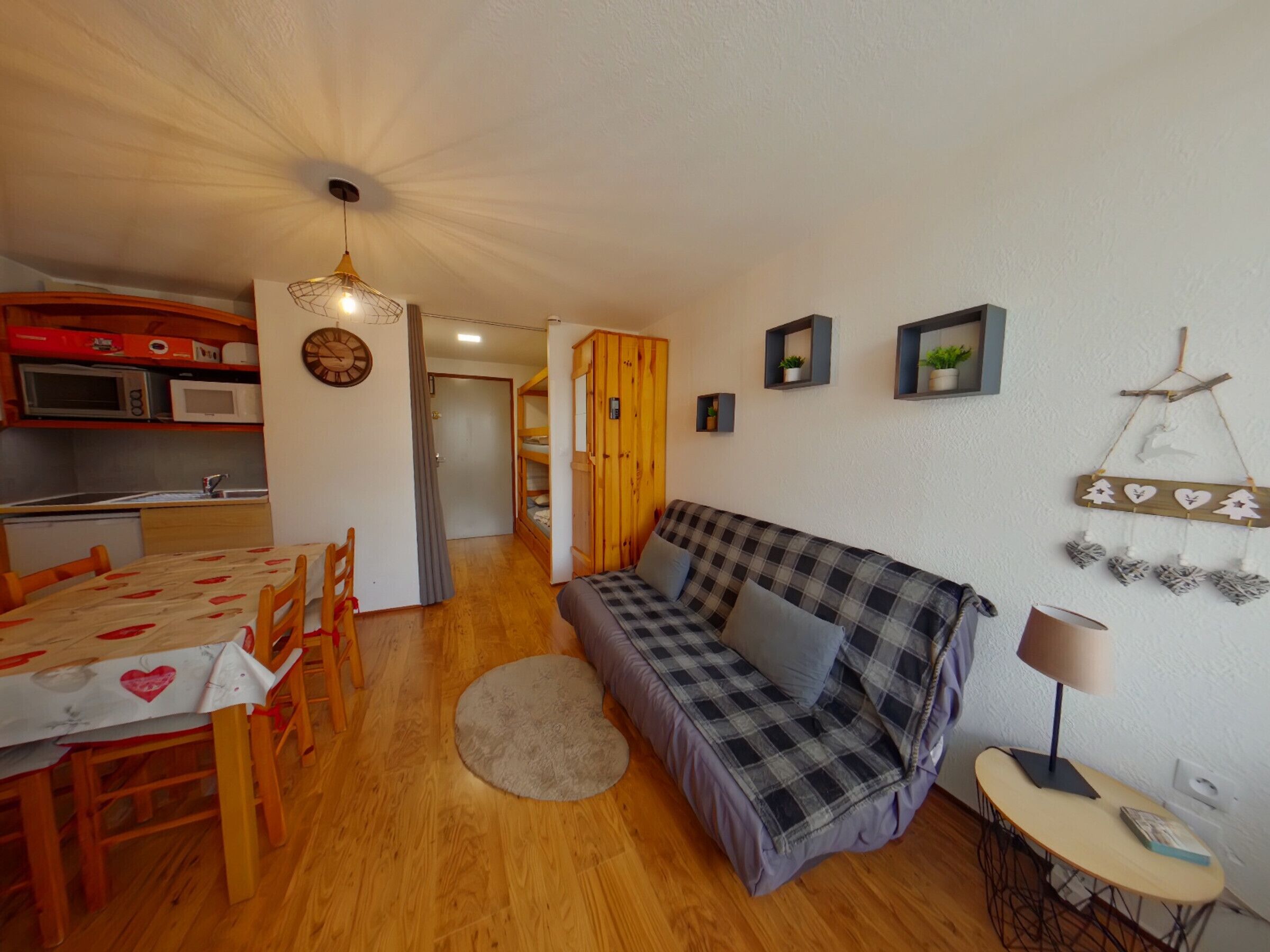 A cozy living room with a sofa, a dining table with chairs, a kitchen area with a microwave, and a small table with a lamp.