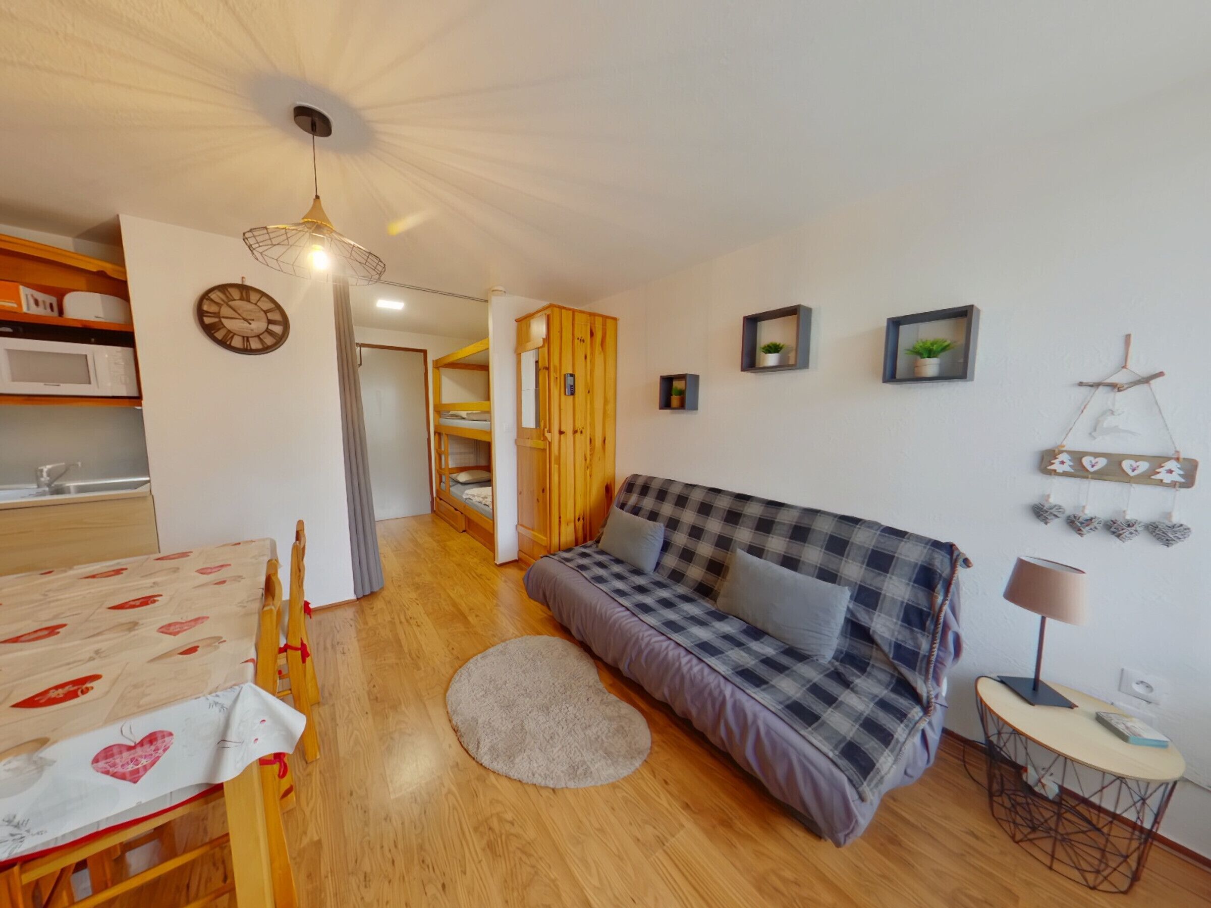 Ein gemütliches Zimmer mit einem karierten Sofa, einem Esstisch mit Stühlen, einem kleinen runden Tisch mit einer Lampe und einem Holzschrank.