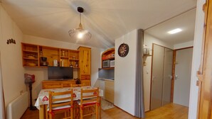 A compact kitchen with wooden cabinets, a dining table with chairs, a television, and a microwave. - Quiet apartment, private parking - 4 guests (Les Rousses)