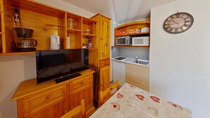 A compact kitchen with wooden cabinets, a microwave, a coffee maker, and a clock on the wall. - Quiet apartment, private parking - 4 guests (Les Rousses)