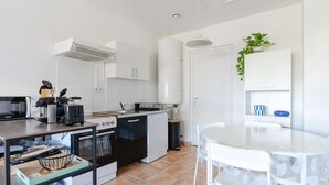 Eine kleine Küche mit Herd, Backofen und Mikrowelle, ein Esstisch mit Stühlen und ein Blumentopf.