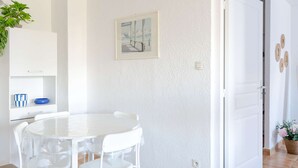 Ein Essbereich mit einem weißen Tisch und Stühlen, einem weißen Schrank mit einer blau-weißen Schüssel, einem gerahmten Bild an der Wand und einer Tür mit Holzverzierungen.