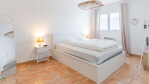Ein Schlafzimmer mit einem Bett, Nachttischlampen, einem Fenster mit Vorhängen und einer Pendelleuchte.