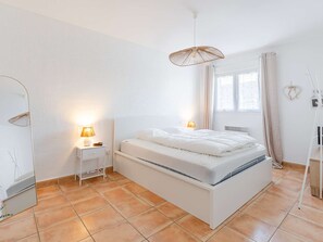 Un dormitorio con cama, lámparas de noche, una ventana con cortinas y una lámpara colgante.