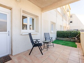 Un patio con dos sillas, una mesa pequeña, una ventana y un seto verde.