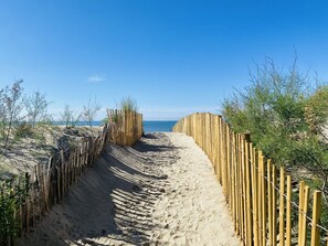 Caminho de areia ladeado por cercas de madeira, em direção ao mar.