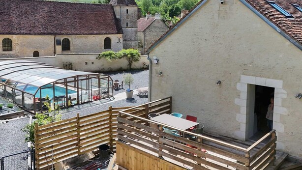 A courtyard with a swimming pool, a wooden deck, and a building with a tiled roof.
