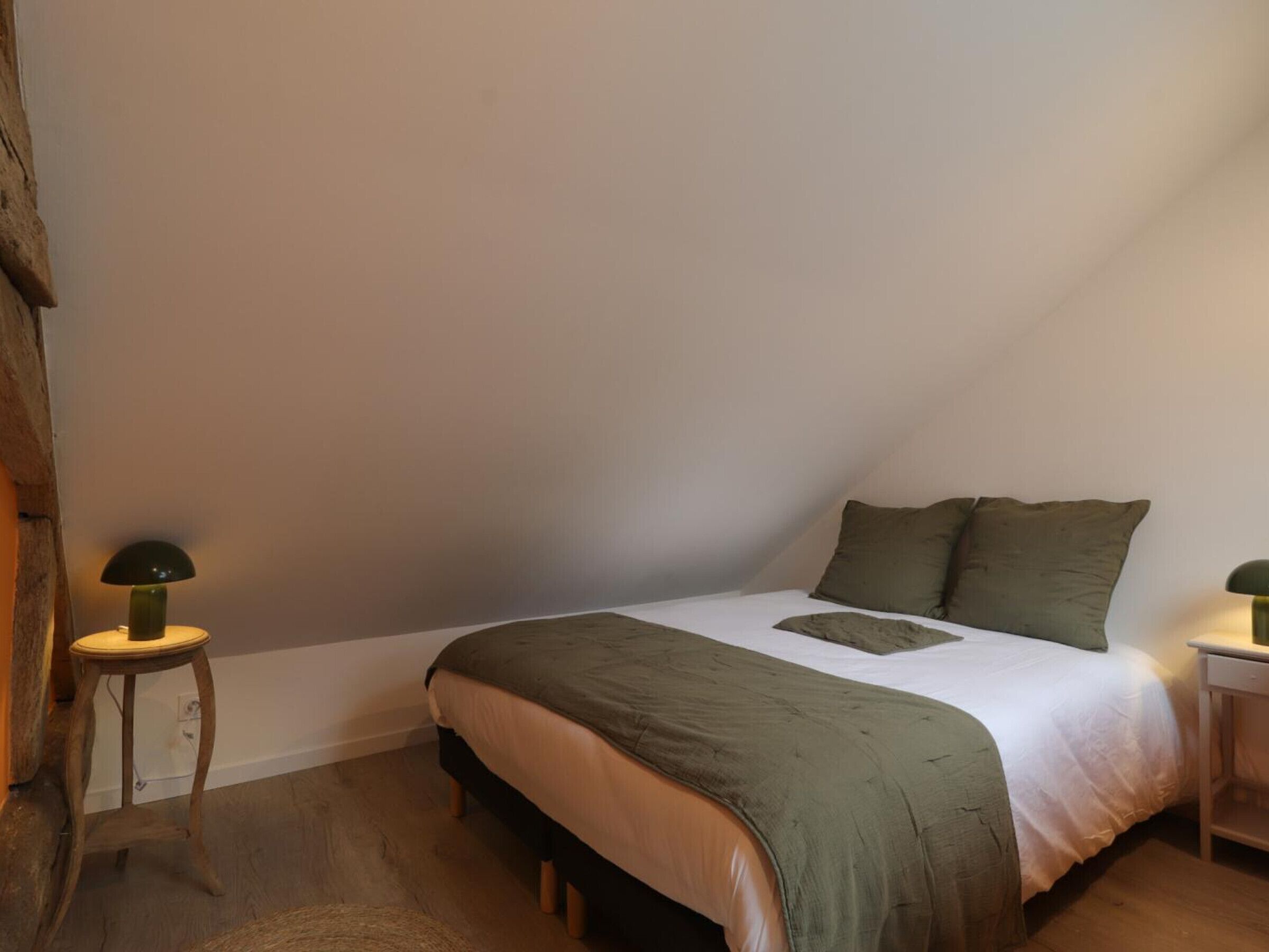 Un dormitorio con una cama, dos mesitas de noche, una lámpara en cada una y suelo de madera.