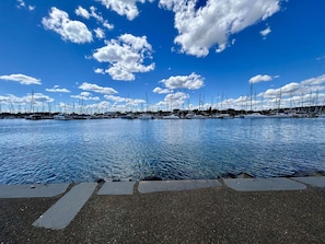 Un port de plaisance où sont amarrés de nombreux voiliers, avec une eau calme et un ciel bleu clair parsemé de quelques nuages.