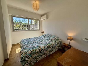 Ein kleines Zimmer mit einem Einzelbett, einem Fenster, einer Nachttischlampe und einem kleinen Tisch.