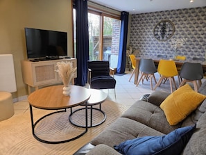 A living room with a sofa, a coffee table, a TV, and a dining area with chairs.