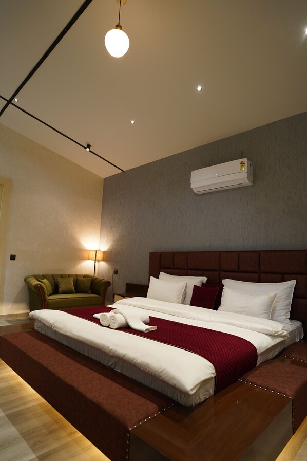 A modern hotel room with a large bed, a green sofa, a bedside lamp, and an air conditioning unit.