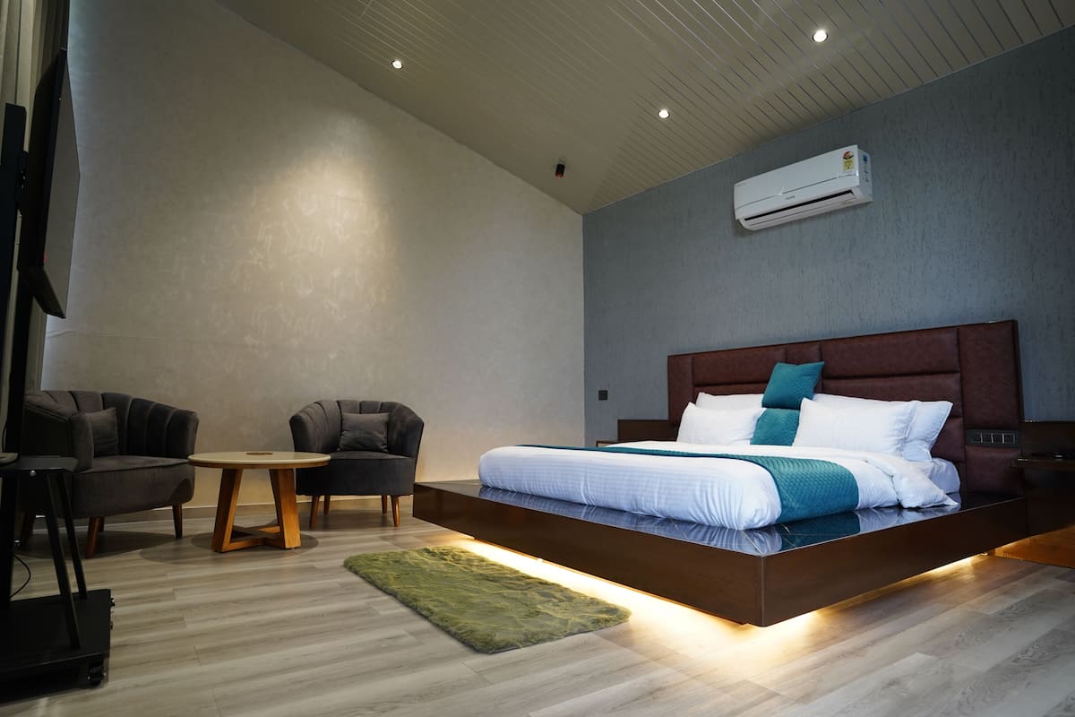 Un dormitorio moderno con una cama grande, una mesita redonda pequeña, dos sillones y un equipo de aire acondicionado en la pared.