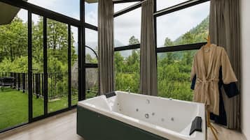 Un baño moderno con una bañera grande, vistas a la vegetación y un balcón con mobiliario exterior.