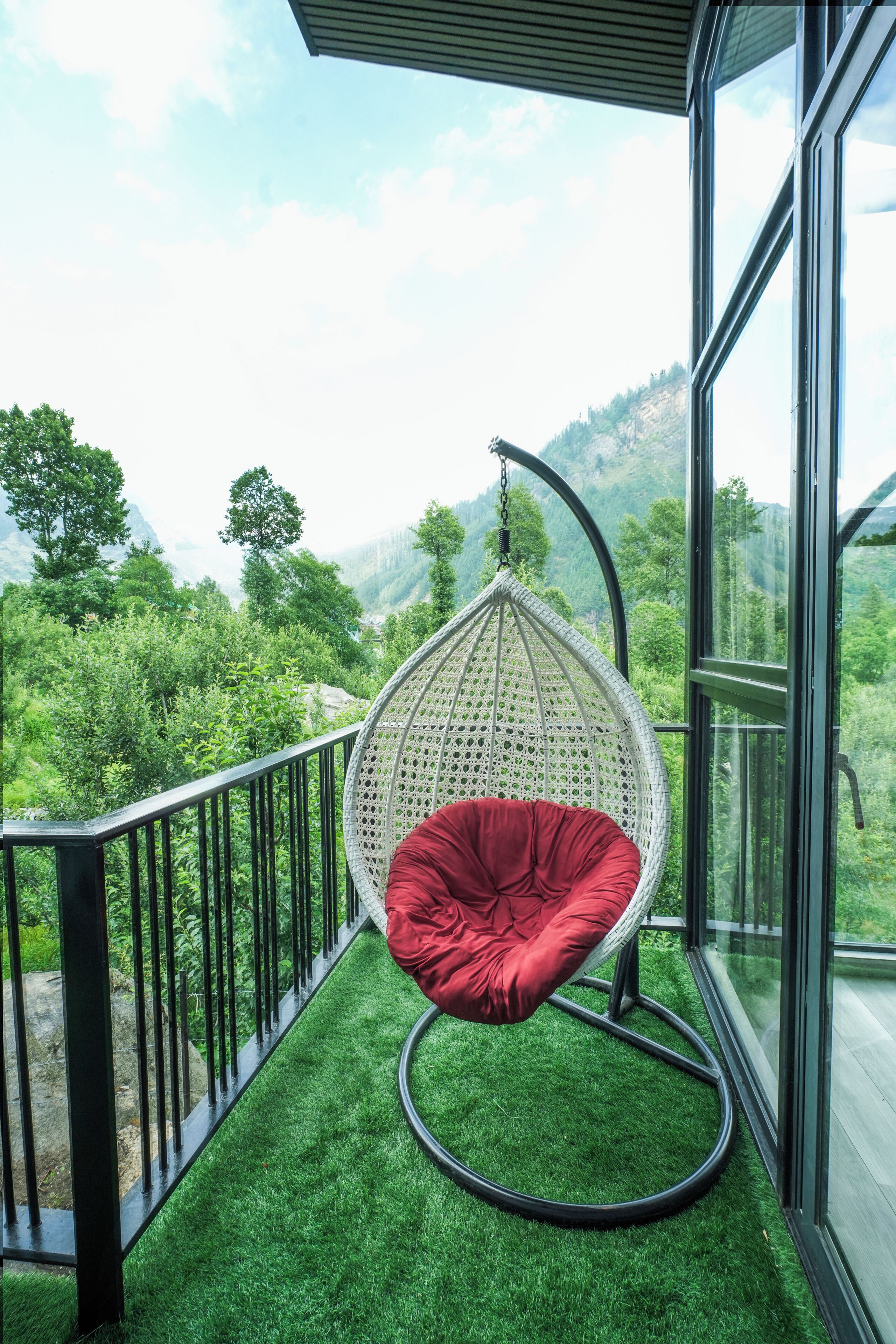 A room with a hanging chair on a balcony with a view of green hills.