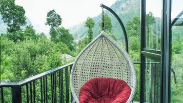A room with a hanging chair on a balcony with a view of green hills.