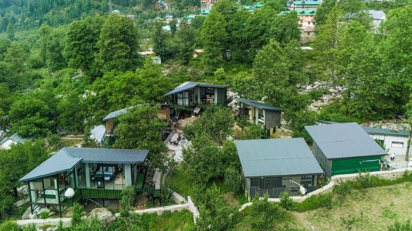 Un ensemble de chalets modernes aux murs de verre, entourés d’une forêt dense et reliés par un étroit sentier.