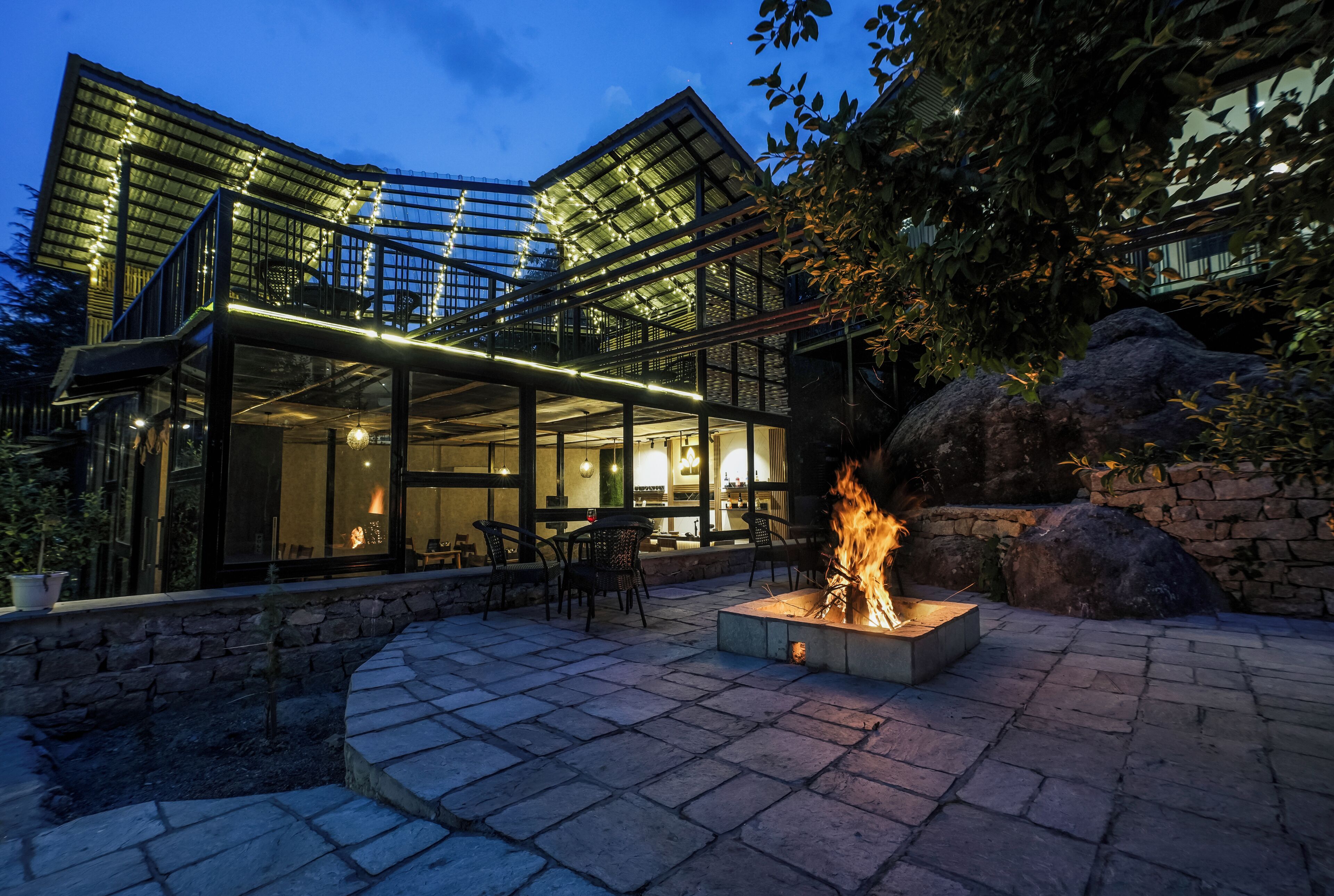 Un edificio moderno con fachada de vidrio, asientos al aire libre y una chimenea exterior.
