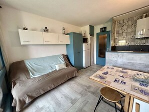 A compact living space with a sofa, a dining table, a kitchen area, and a refrigerator. - Studio with garden view - 4 guests (Cap d'Agde)