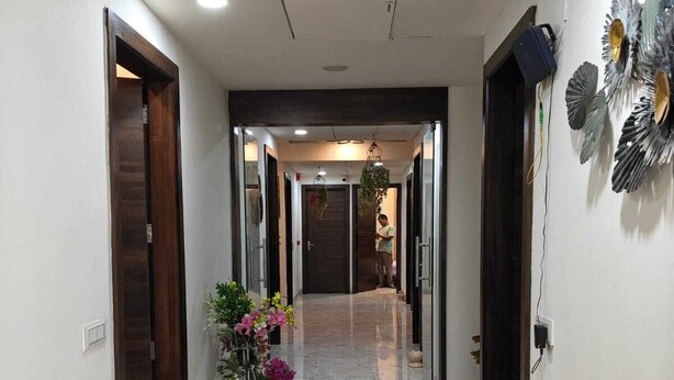 A hallway with marble flooring, wooden doors, and a potted plant with flowers. - Crown Palace Hotel & Restaurant (Hapur)