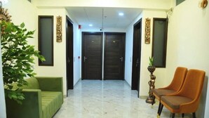 A hotel lobby with a green sofa, an orange chair, marble flooring, and double doors. - Crown Palace Hotel & Restaurant (Hapur)