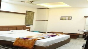 A hotel room with a bed, bedside tables, a ceiling fan, and a window with curtains. - Crown Palace Hotel & Restaurant (Hapur)