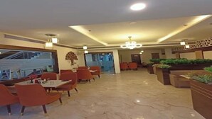 A hotel lobby with marble flooring, orange chairs, and tables, a staircase, and a reception area. - Crown Palace Hotel & Restaurant (Hapur)