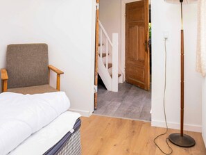 Una habitació amb un llit, una cadira, una làmpada de peu i una escala que mena a una altra habitació.