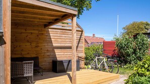 A wooden cabin with a covered porch, a bicycle, and a red structure in the background. - 4 Star Holiday Home in Samso (Samsø)