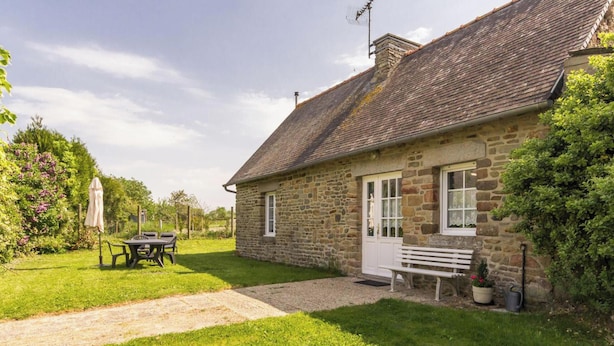 Une maison en pierre avec une porte blanche, un banc et une table dans la cour.