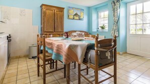 Un coin repas avec une table dressée pour quatre personnes, des chaises en bois, un buffet et une fenêtre avec des rideaux.