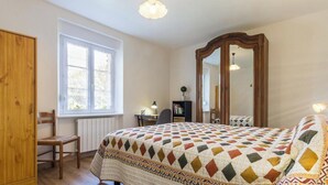 Une chambre avec un grand lit, une chaise en bois, un bureau, un miroir et une fenêtre.
