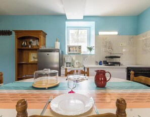 A dining table set with plates, a pitcher, and a glass, in a kitchen with a refrigerator, microwave, and stove. - House in Céaux, distant view - 2 guests (Céaux)