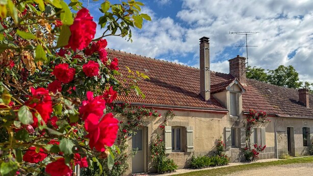 Une maison avec un toit recouvert de tuiles rouges, une cheminée et une allée gravillonnée.