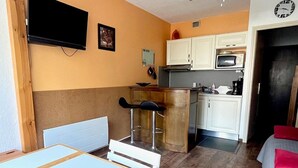 Une cuisine compacte avec des meubles blancs, un four à micro-ondes et un petit tabouret de bar.
