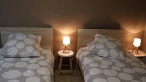 Zwei Betten mit passenden Kopfteilen und Bettwäsche mit einem kreisförmigen Muster, jeweils mit einer kleinen Nachttischlampe.