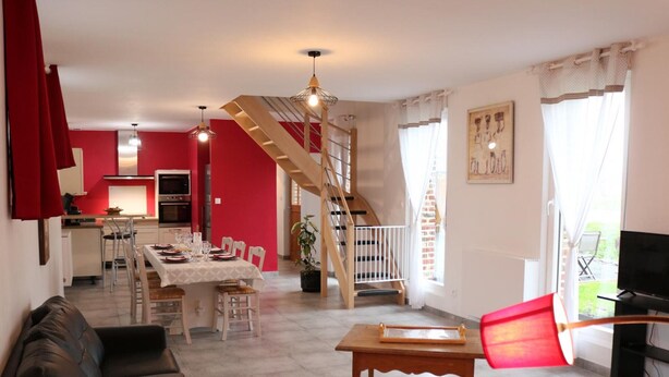Ein Wohnzimmer mit einer Couch, einem Essbereich mit Tisch, einer Treppe und einer Küche im Hintergrund.