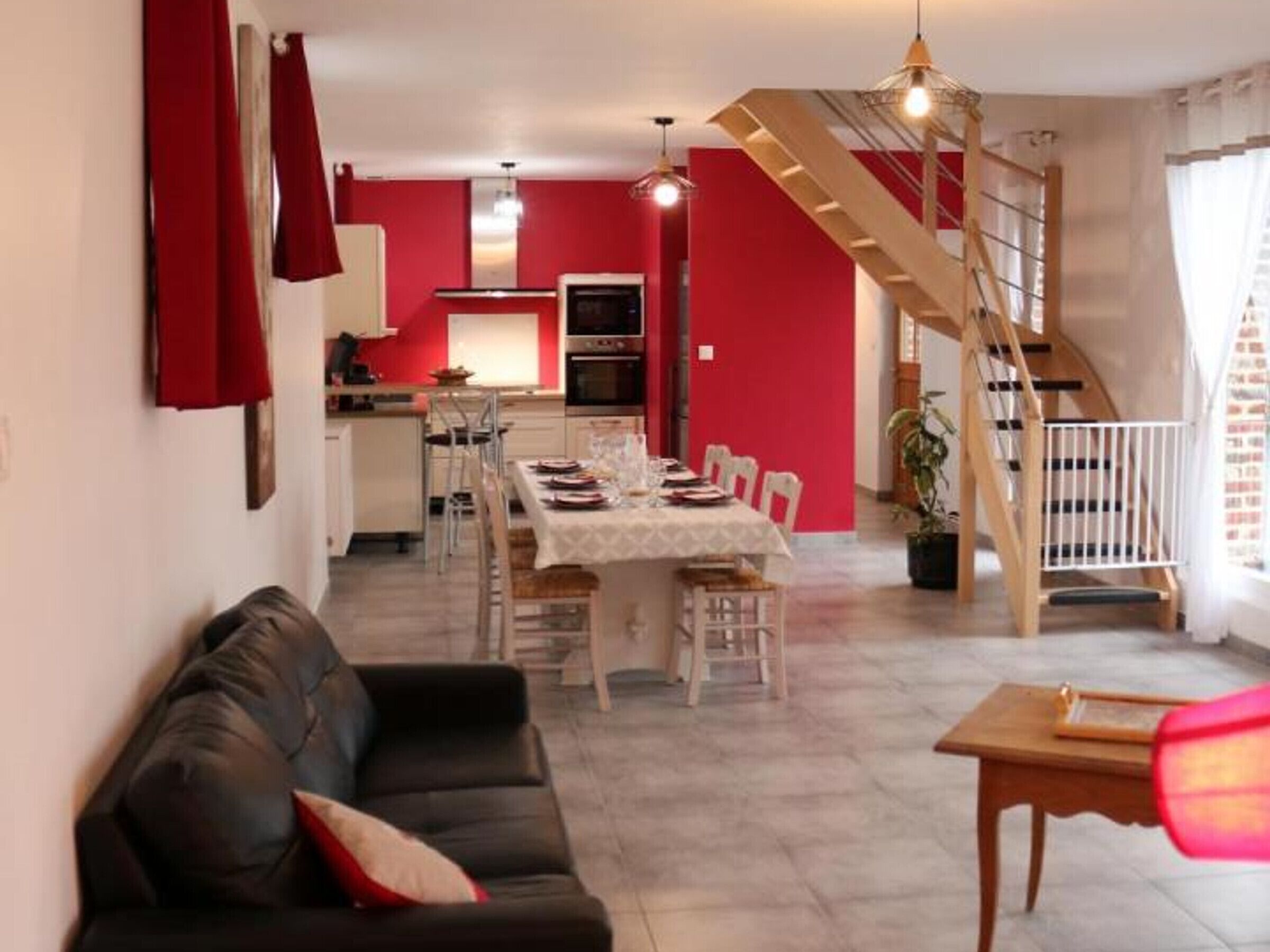 Ein Essbereich mit Tisch für vier Personen, eine Treppe, eine Küche und ein Wohnzimmer mit Sofa.