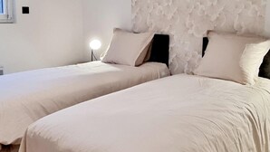 Deux lits simples avec du linge de lit blanc, une table de chevet avec une lampe et un mur à motifs.