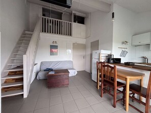 A two-story apartment with a staircase, a sofa, a wooden dining table with chairs, a kitchen area, and a small wooden bench. - Apartment with pets - 4 guests (Moliets-et-Maa)